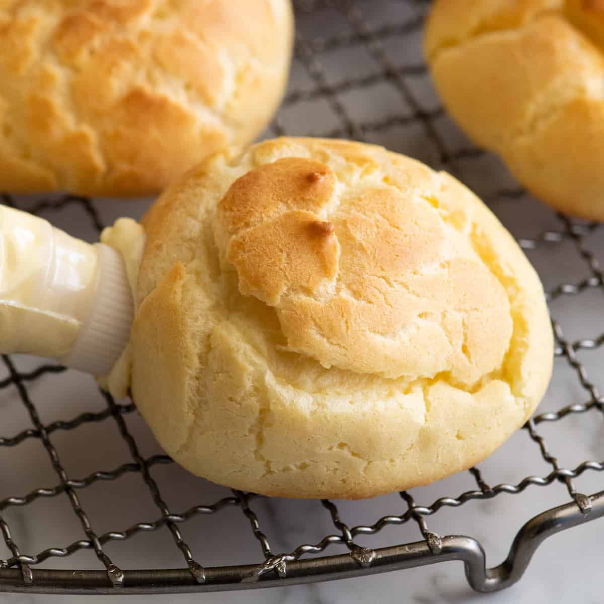 front view showing a piping bag filling a pastry puff with eclair filling