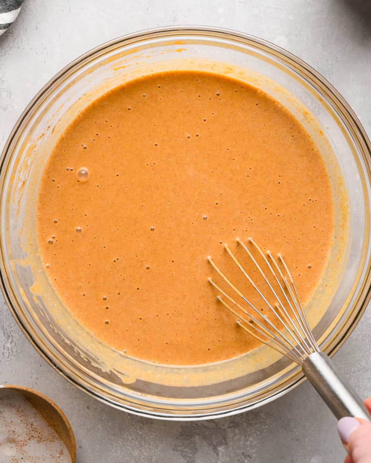 pumpkin pie filling ingredients being whisked together in a glass bowl on a gray surface 