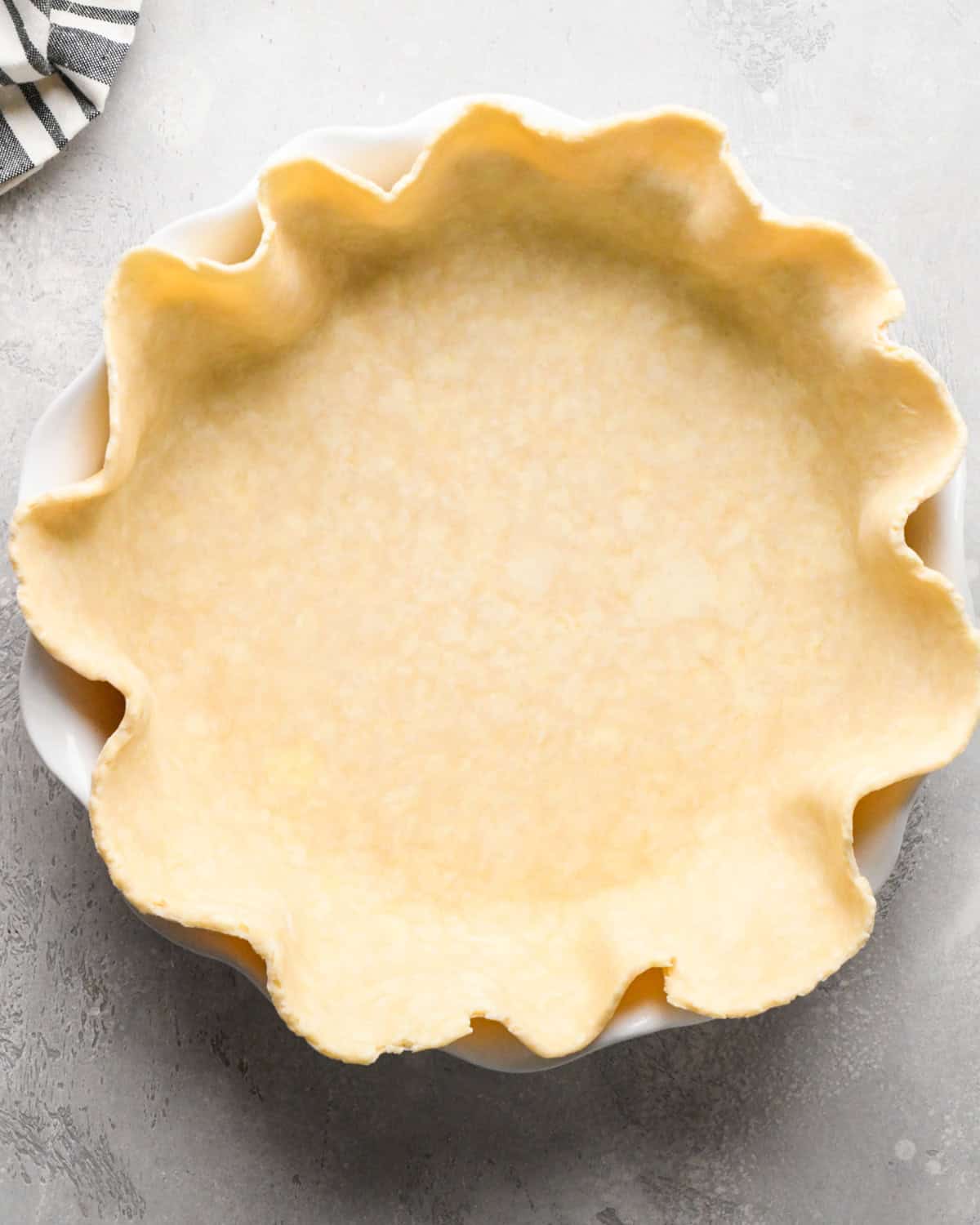 rolled out pie crust down in a white ceramic pie dish on a gray surface 