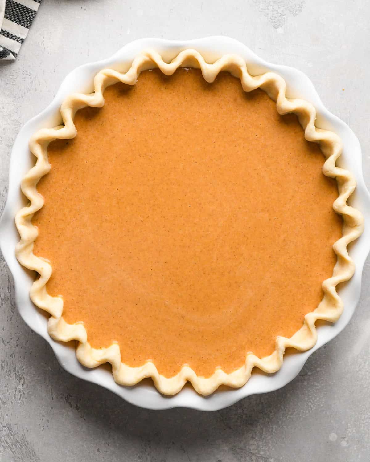 pumpkin pie in a white pie dish before baking on a gray surface 