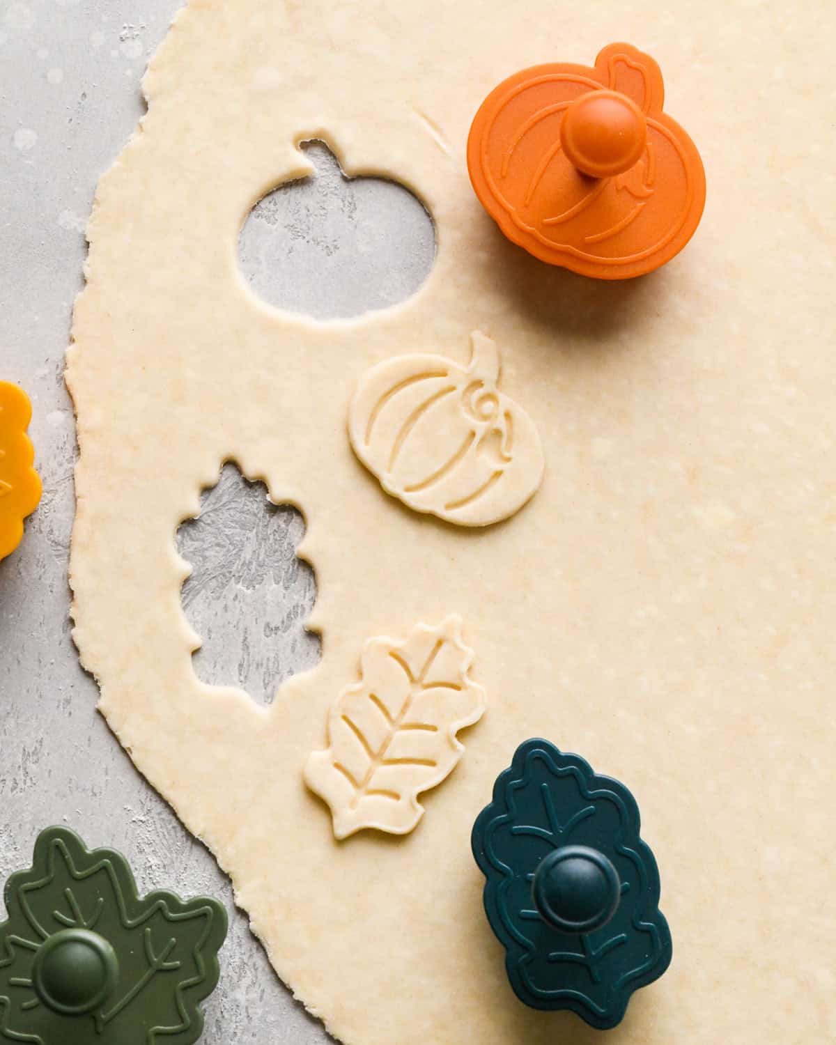 pie crust dough rolled out with pumpkin and leaf pie crust cutters cutting shapes out of the dough