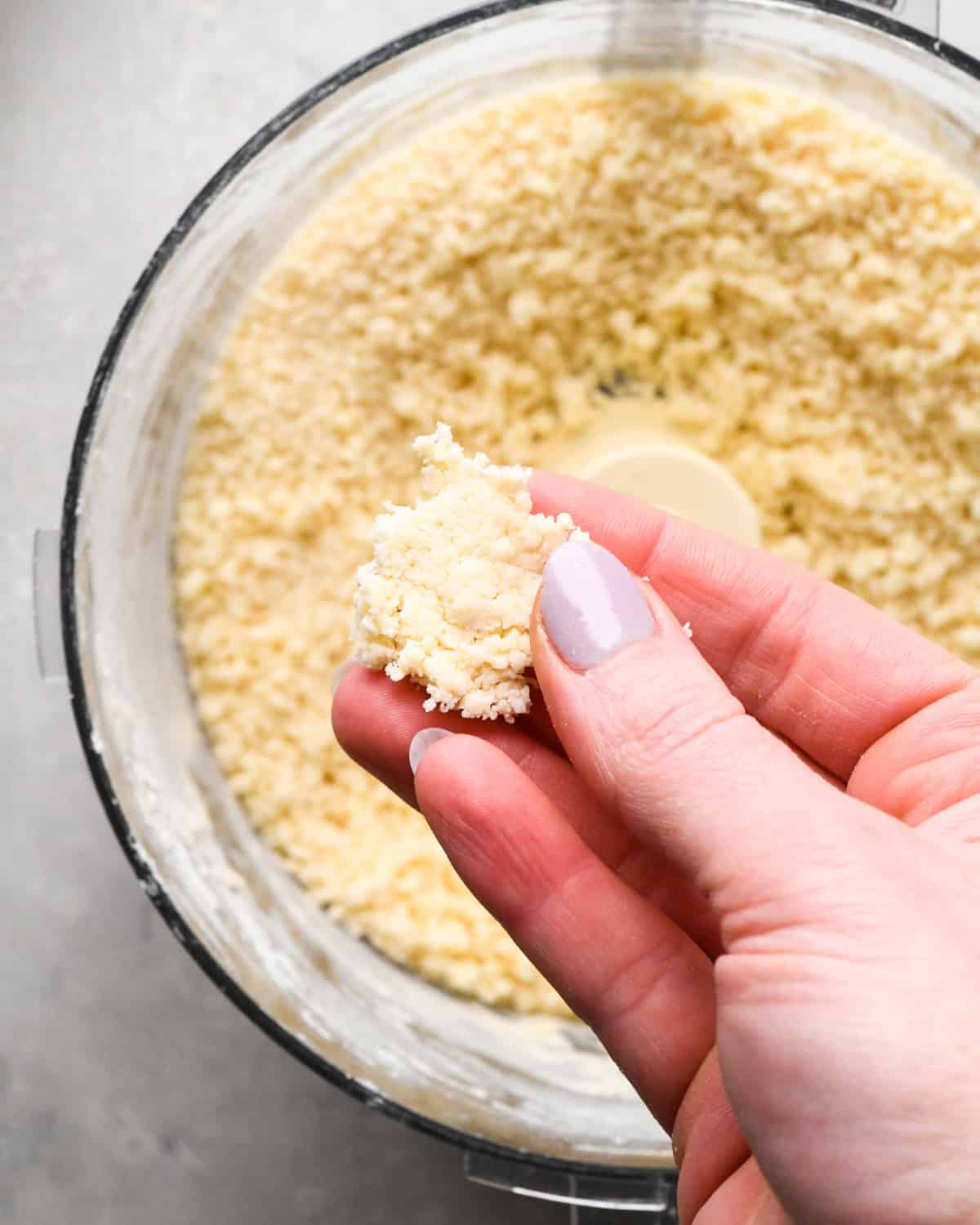 a hand pinching pumpkin pie crust dough together over a food processor