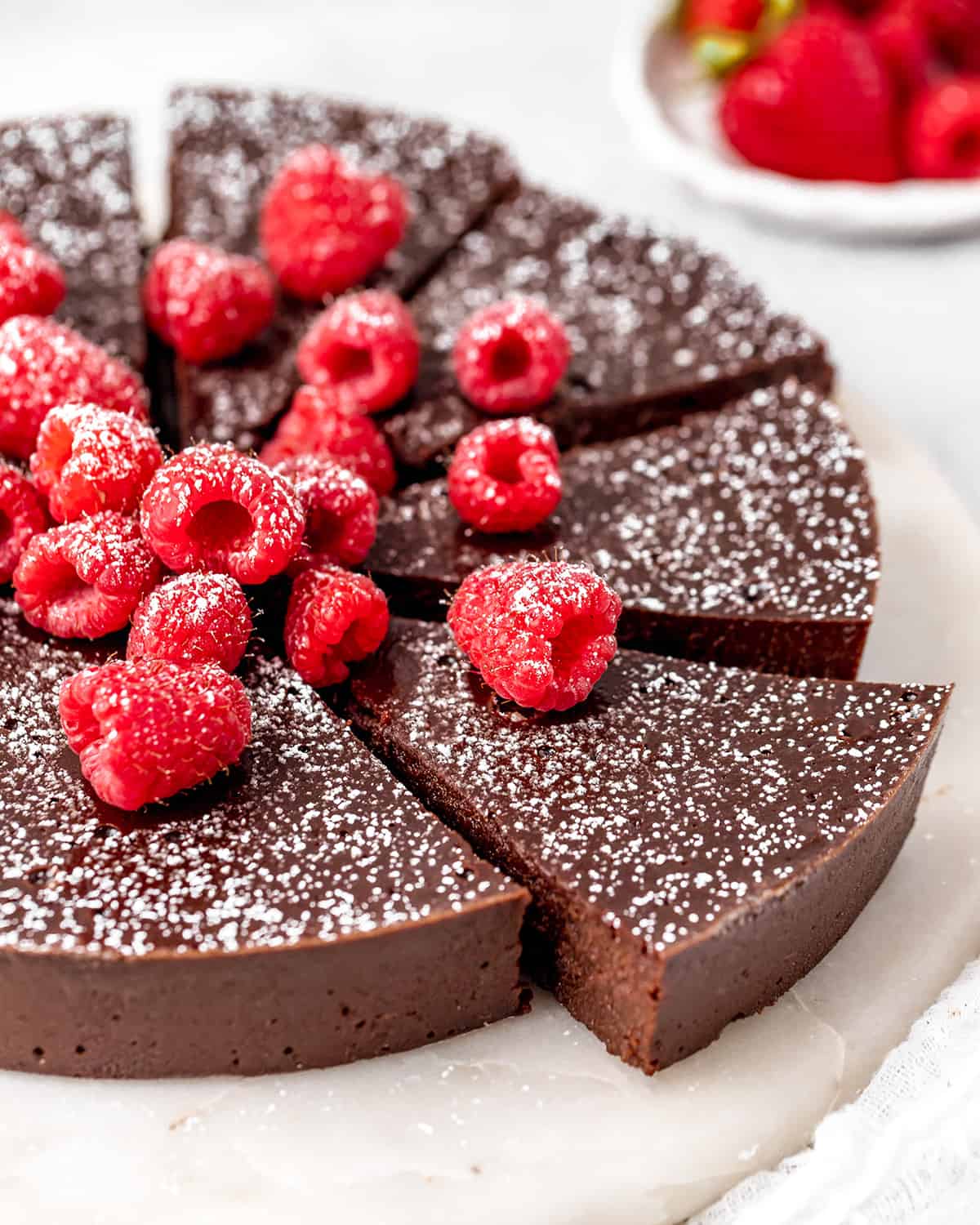 a Flourless Chocolate Cake with 4 slices cut dusted with powdered sugar topped with raspberries 