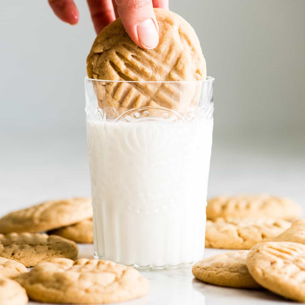 front view of a hand dipping a peanut butter cookie into a glass of milk