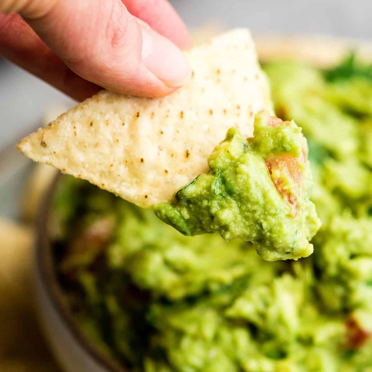 up close front view of a hand holding a chip with guacamole on it