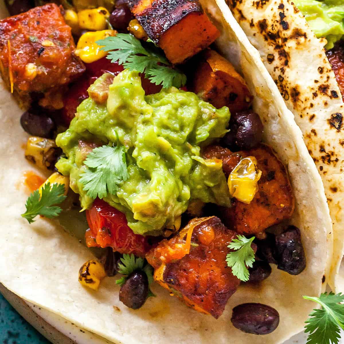 close up photo of a dollop of guacamole recipe on top of a black bean sweet potato taco garnished with cilantro