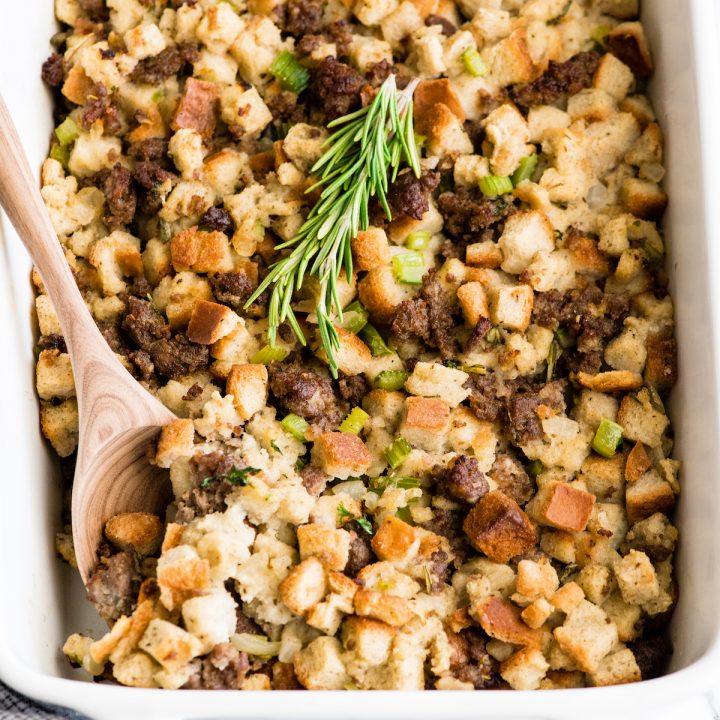 overhead view of sausage stuffing with rosemary on top and a spoon taking a scoop