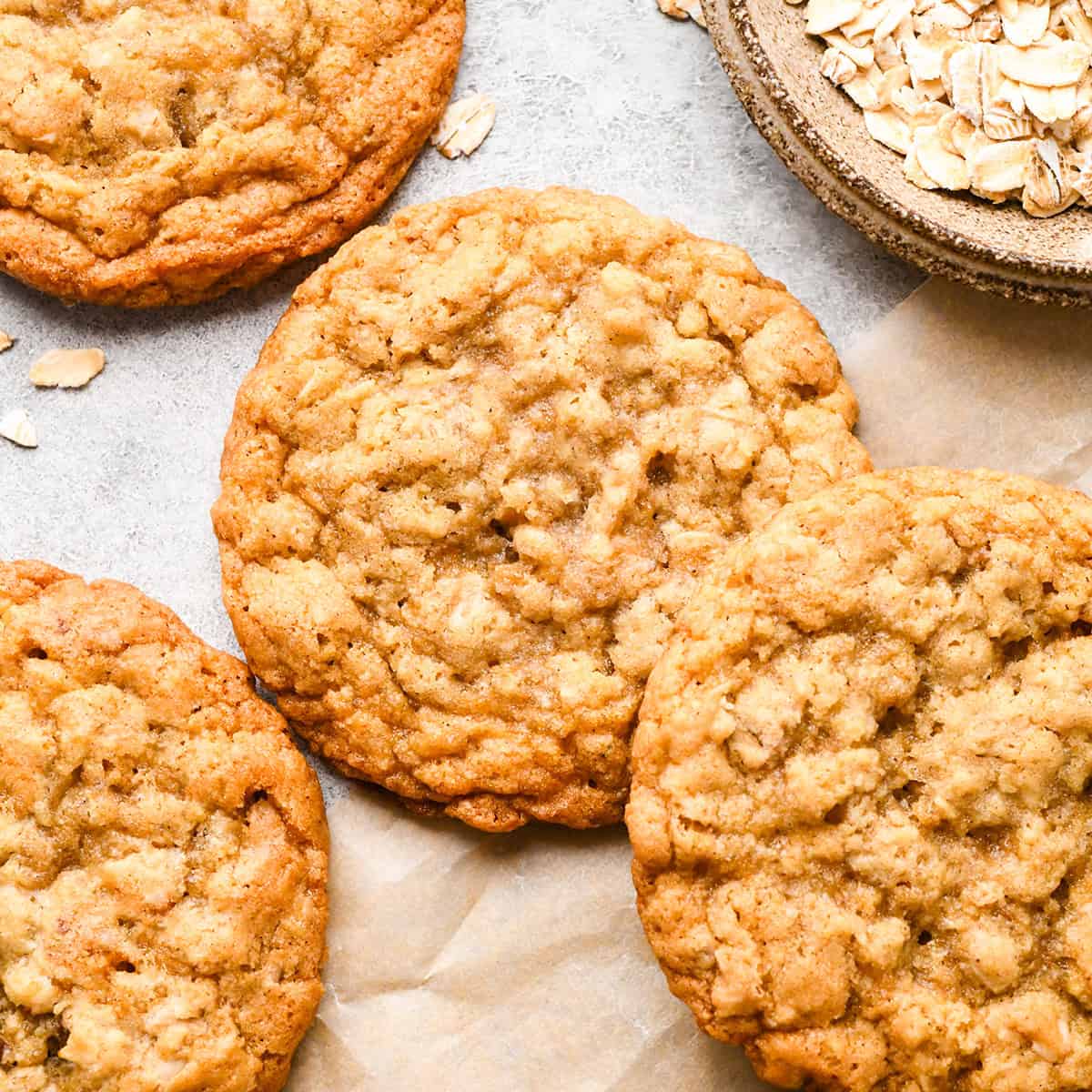 four oatmeal cookies on parchment paper next to a bowl of raw oats