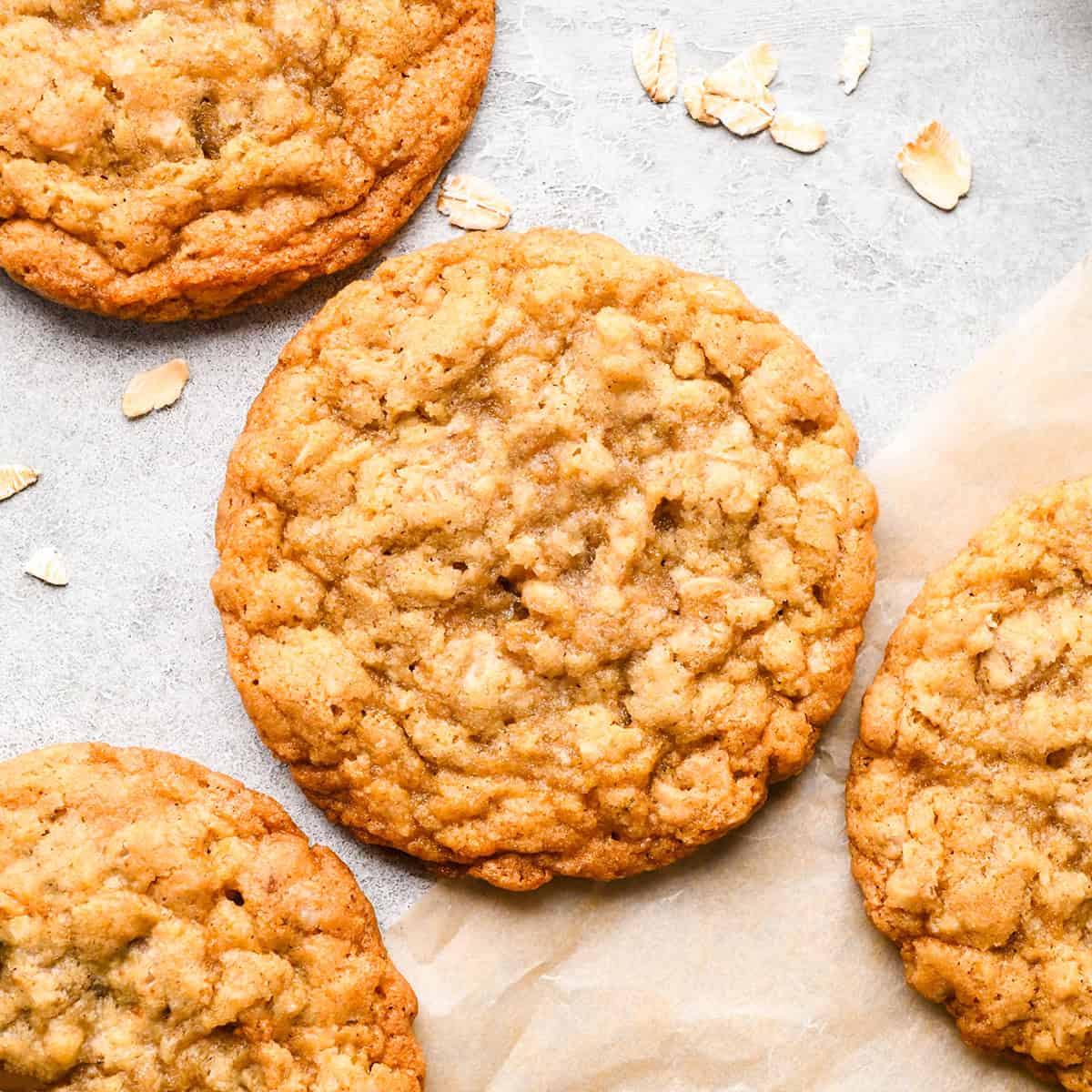 four oatmeal cookies on parchment paper next to a bowl of raw oats