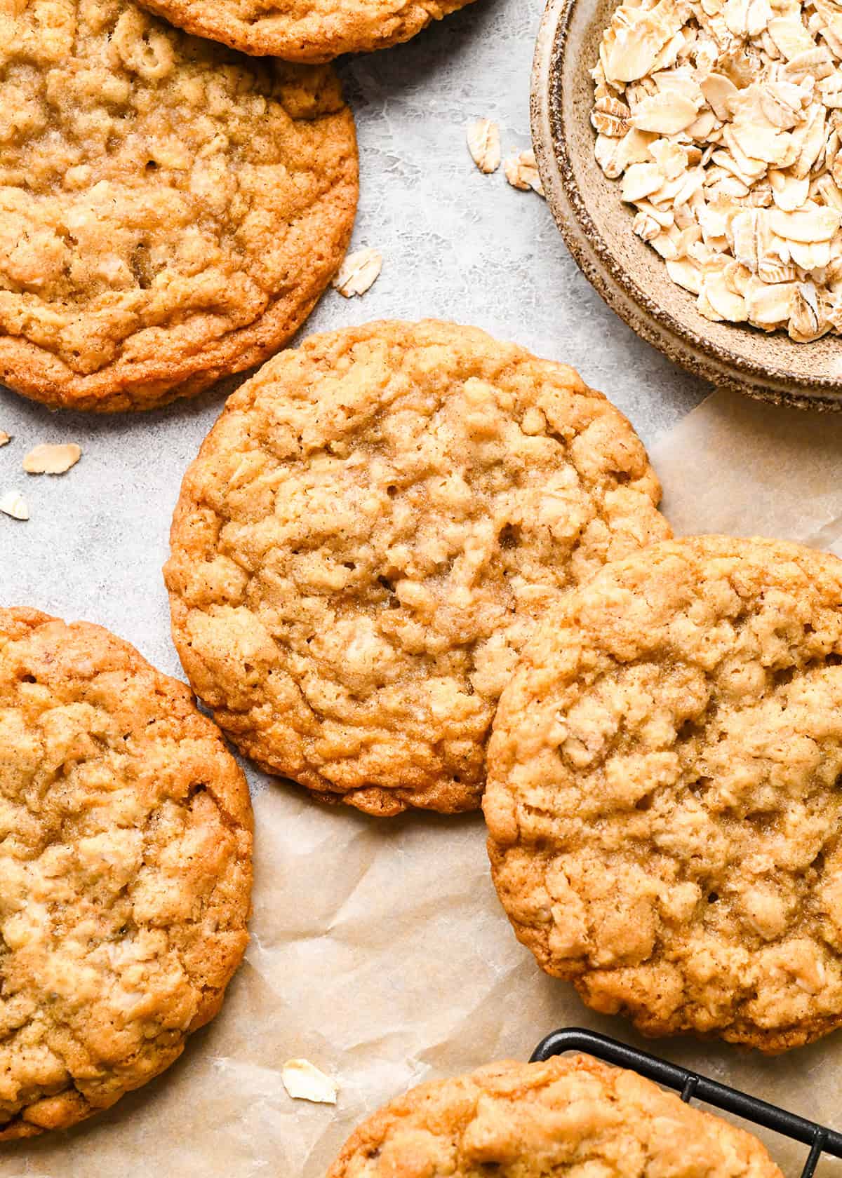 six oatmeal cookies on parchment paper next to a bowl of raw oats