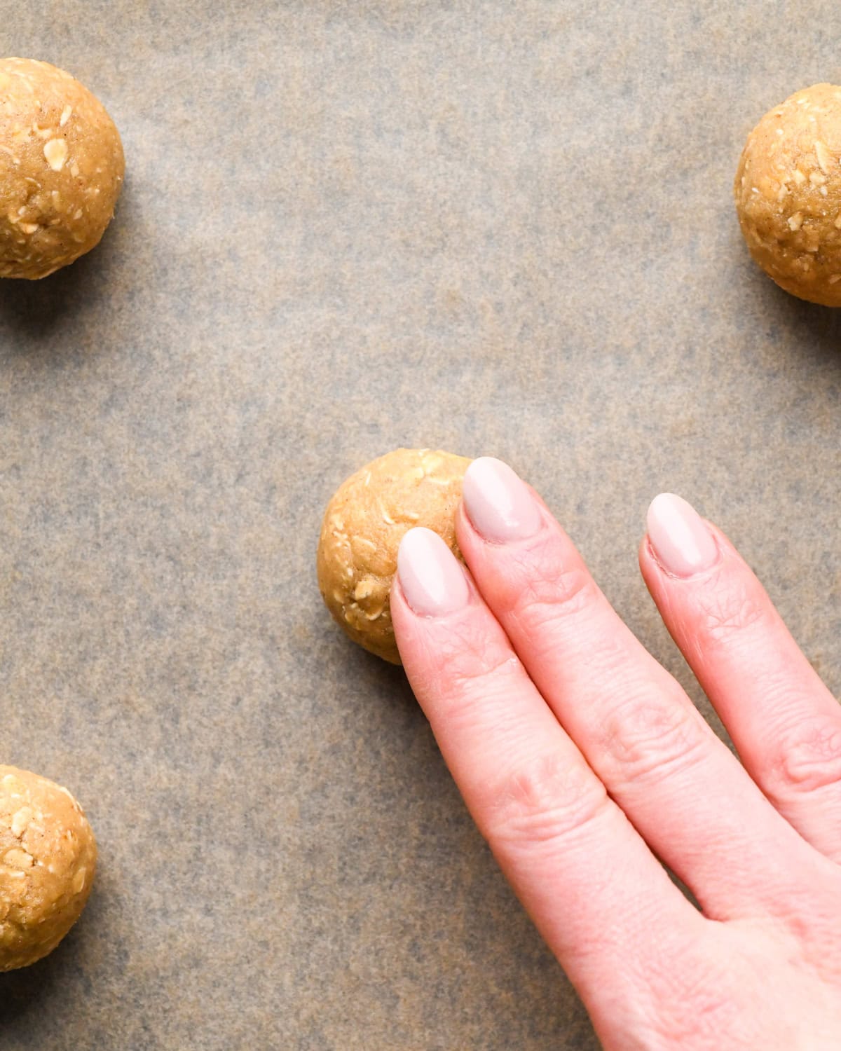 a hand pressing down the top of a cookie dough ball