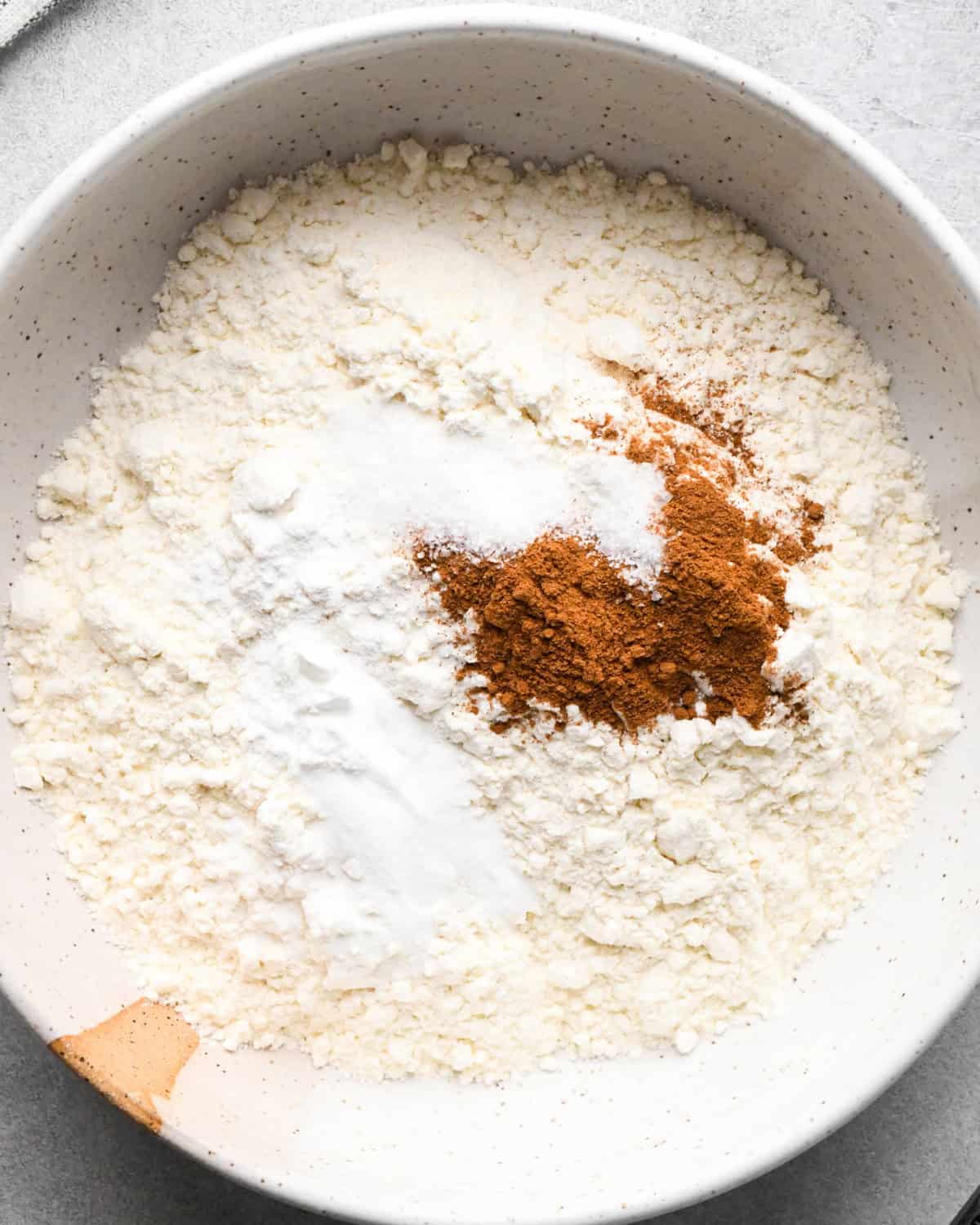 a bowl of flour, salt, baking soda, baking powder and cinnamon before stirring