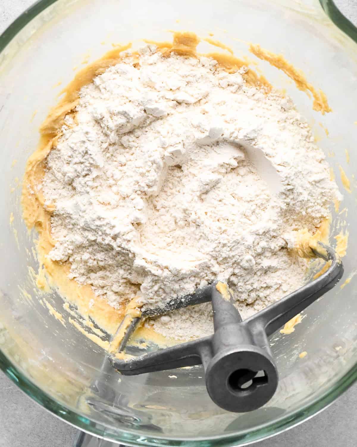 dry ingredients being added to the beaten wet mixture in a mixer with the paddle attachement, preparing oatmeal cookies.
