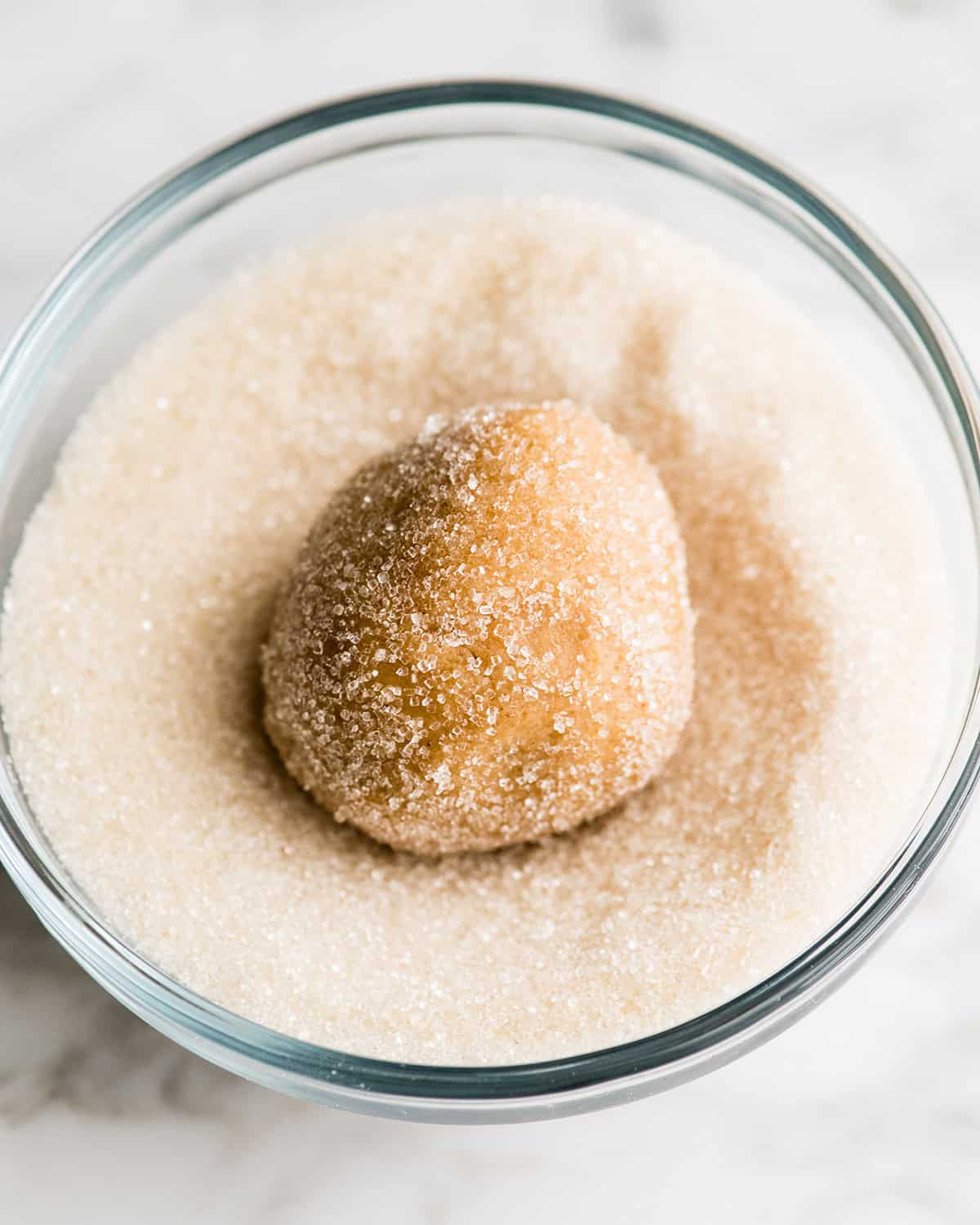 making peanut butter blossoms - cookie dough ball in a glass bowl of sugar being coated with the sugar