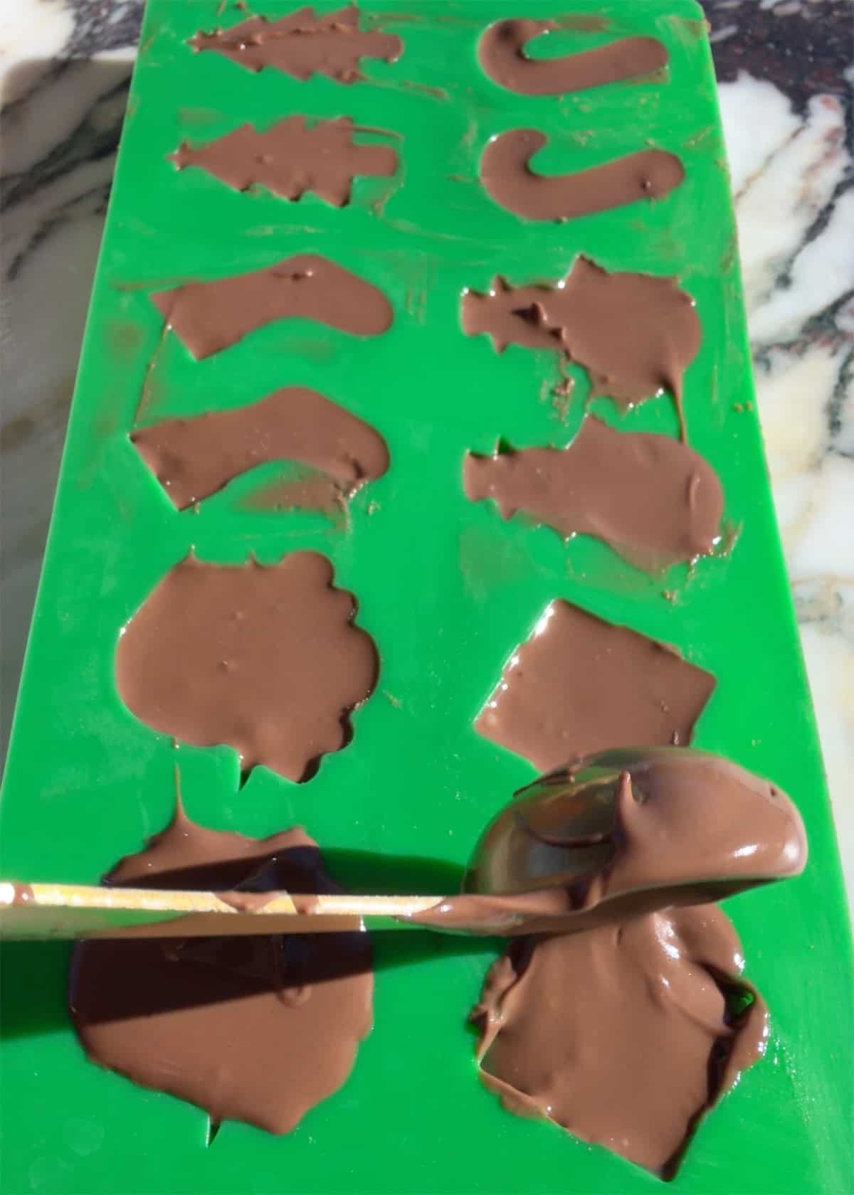 making peanut butter blossoms - melted chocolate being put into a green Christmas silicone candy omld