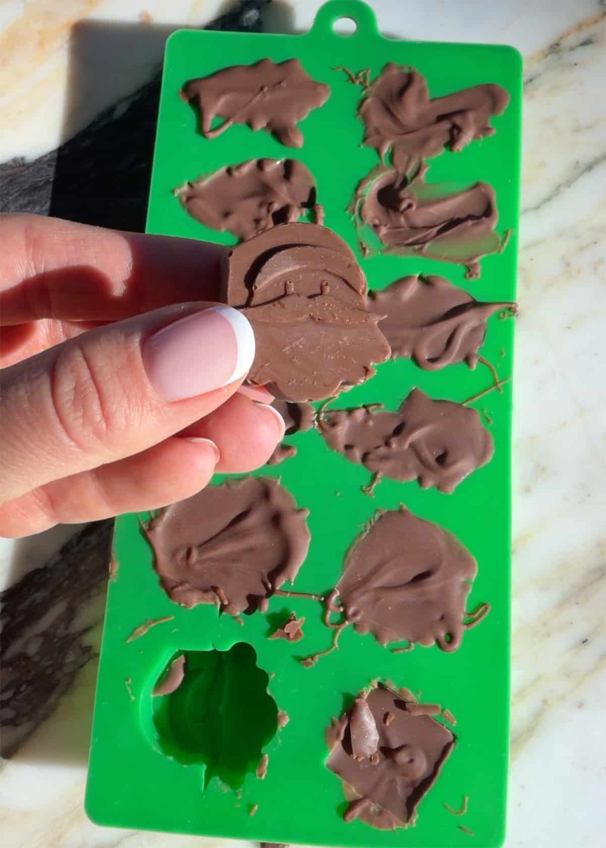 making peanut butter blossoms - a frozen chocolate Santa being held over a green silicone mold
