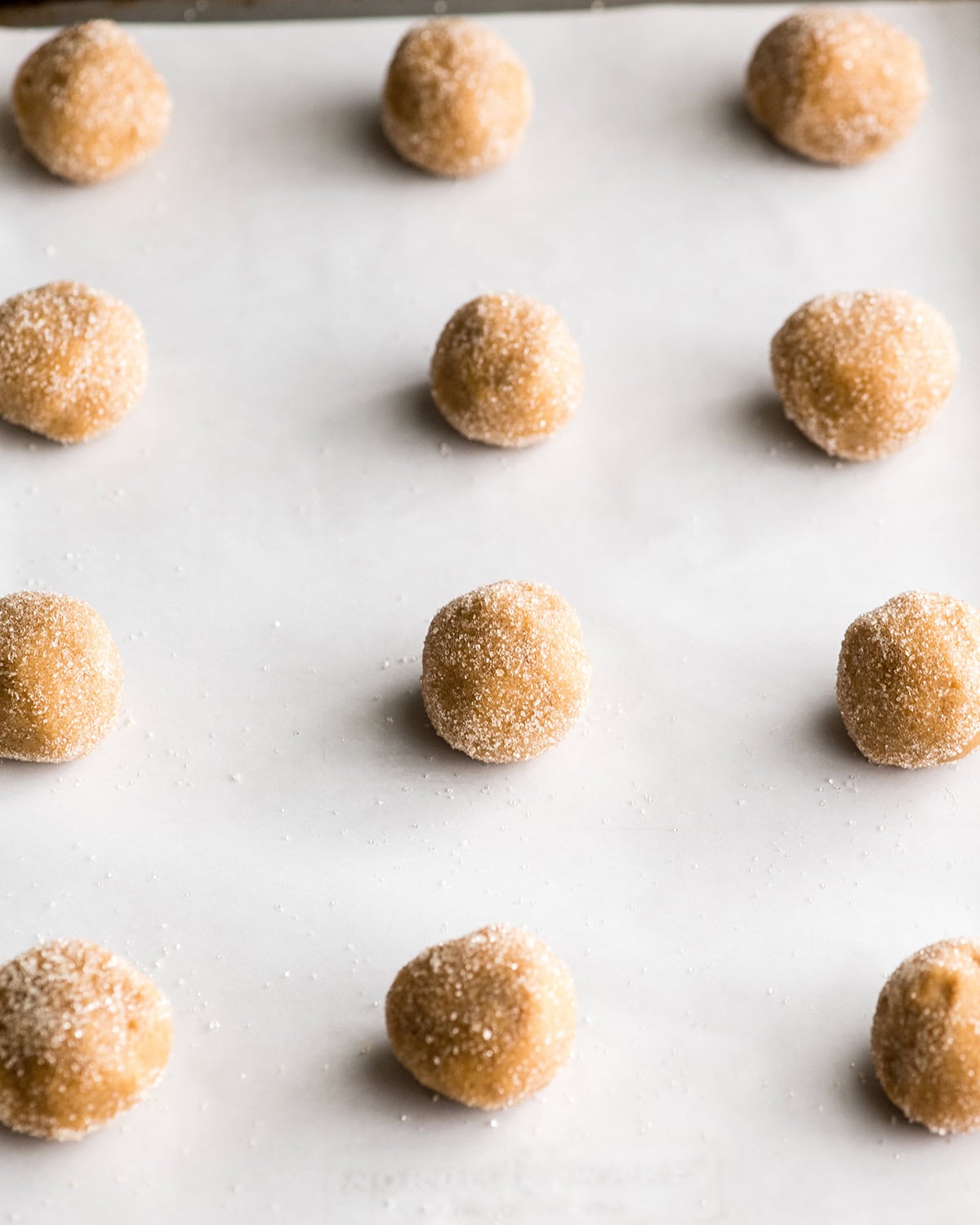 making peanut butter blossoms - 12 sugar-coated cookie dough balls on a baking sheet lined with parchment paper before baking