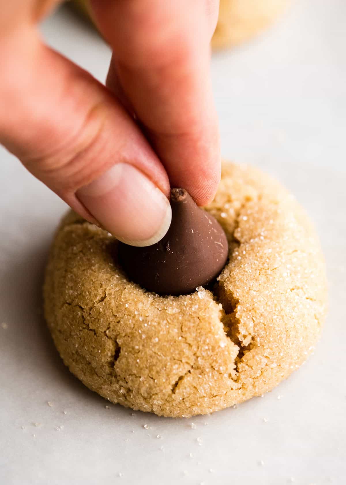 making peanut butter blossoms - a hand pressing a frozen chocolate kiss into the top of a baked peanut butter blossom cookie