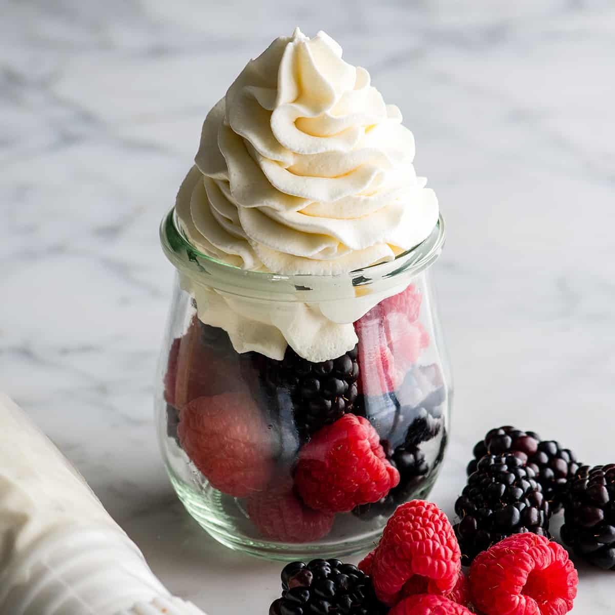  homemade whipped cream piped on top of fresh berries in a glass jar