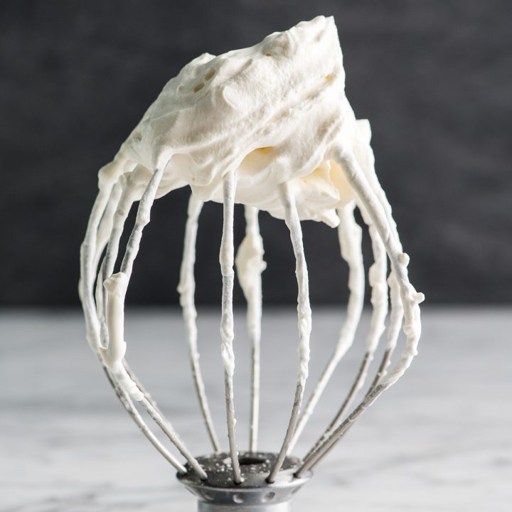 front view of a wire whisk with a stiff peak of homemade whipped cream on it