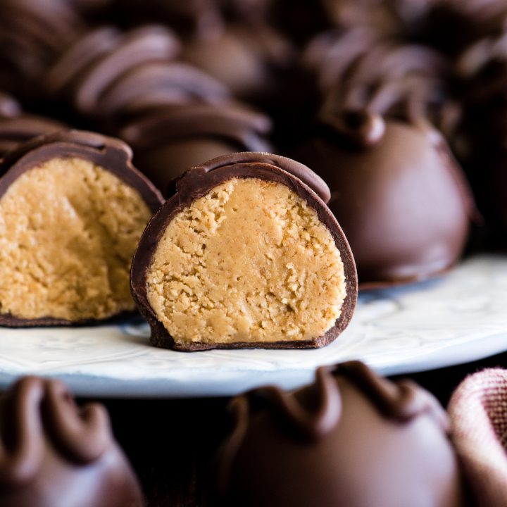 front view of a No-Bake Chocolate Peanut Butter Ball cut in half standing up on a plate surrounded by other peanut butter balls