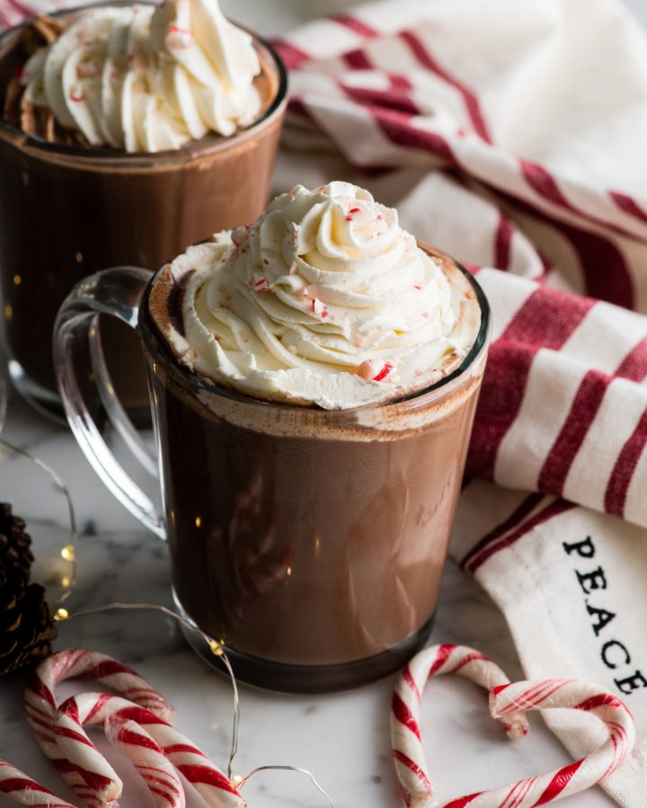 front view of two mugs of peppermint hot chocolate topped with whipped cream and crushed candy canes