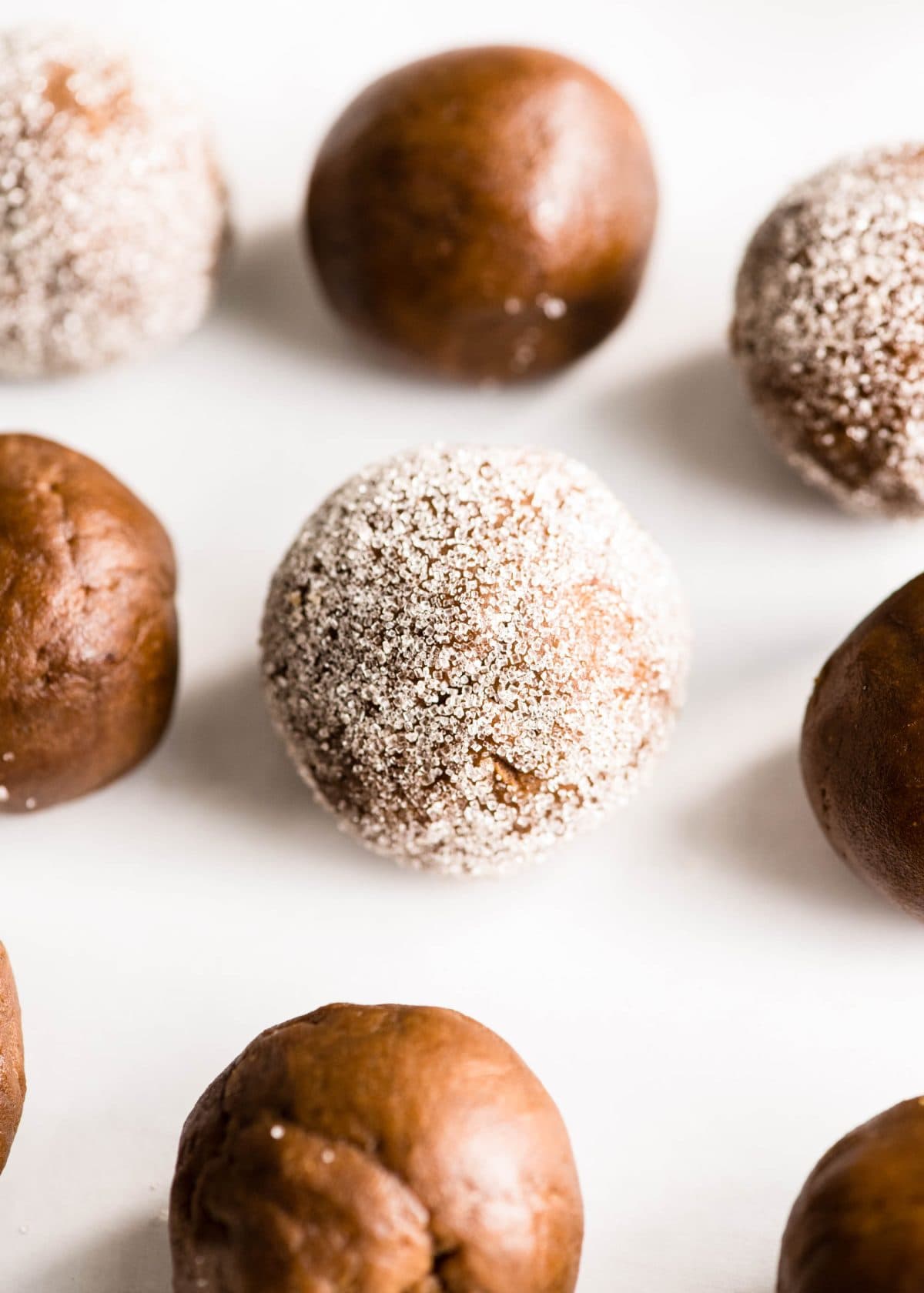 7 balls of easy gingerbread cookies dough, 3 have been rolled in granulated sugar. they're all on a baking sheet lined with white parchment paper