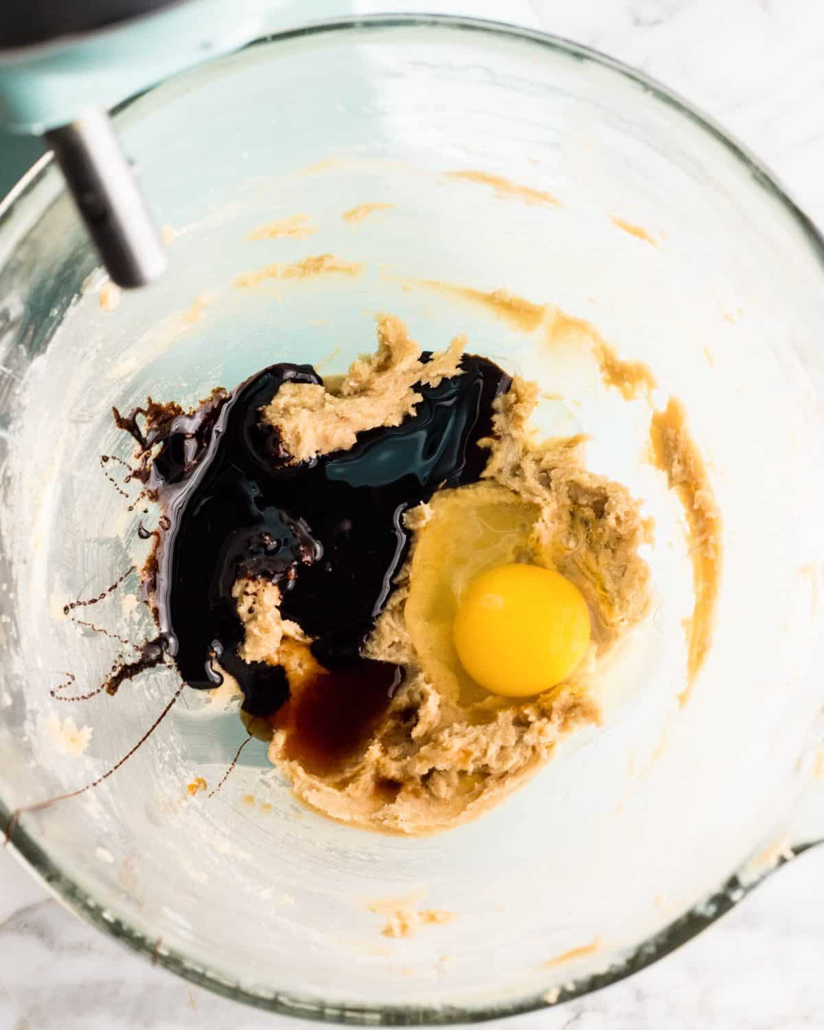 making easy gingerbread cookies - molasses, egg and vanilla added to the beaten butter/sugar mixture in a glass mixing bowl of a light blue standing mixer before beating together