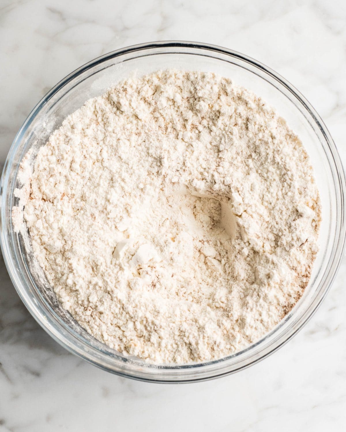 making soft gingerbread cookies - flour, salt, baking soda, cinnamon, ginger, and cloves in a glass bowl on a marble surface after mixing together