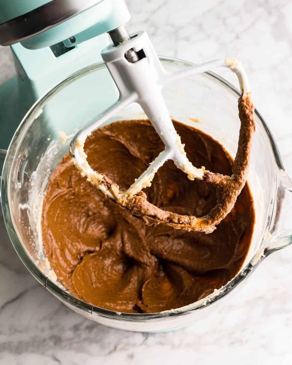 making easy gingerbread cookies - molasses, egg and vanilla added to the beaten butter/sugar mixture in a glass mixing bowl of a light blue standing mixer fitted with the paddle attachment after beating together
