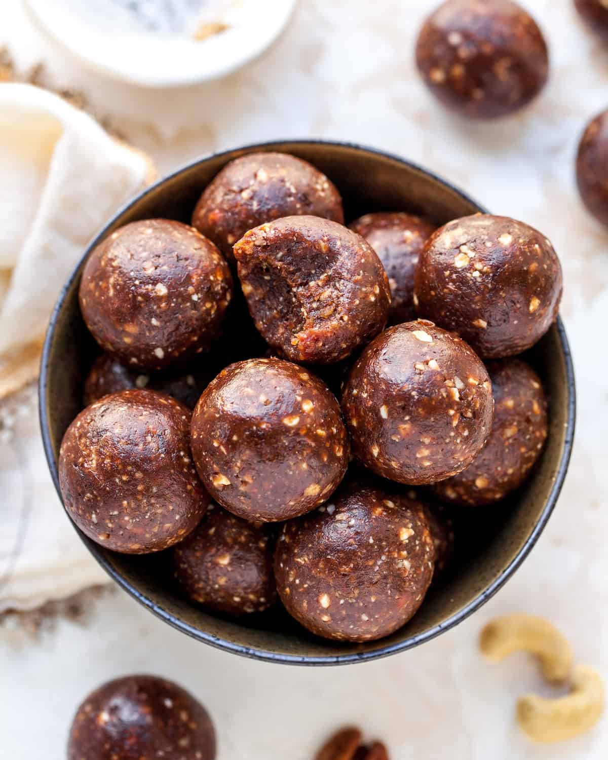 Chocolate Date Energy Balls in a bowl, one has a bite taken out of it 