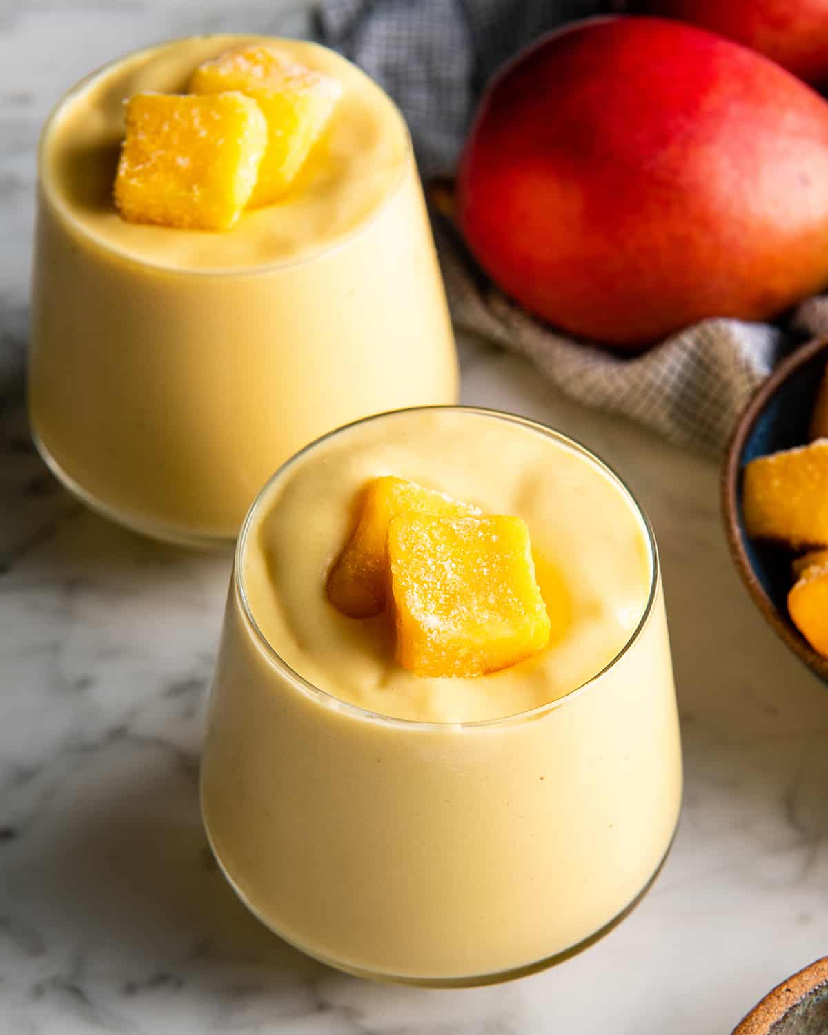 two glasses of mango smoothie with mango chunks on top