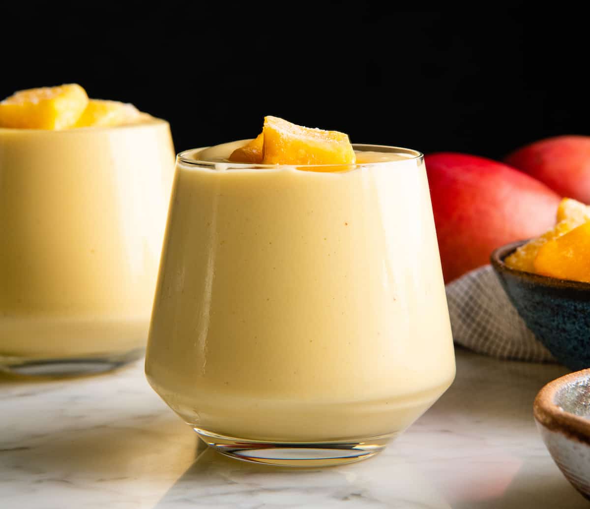 front view of two glasses filled with mango smoothie with frozen chunks of mango on top