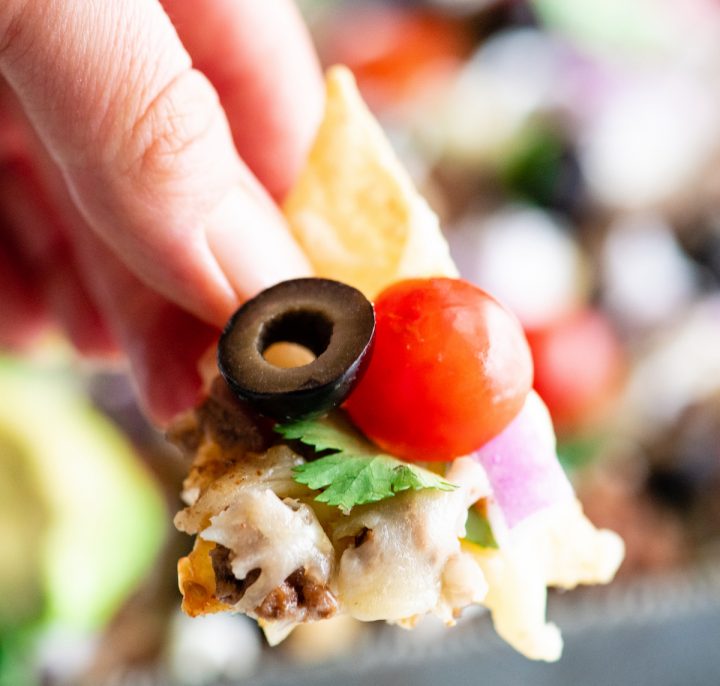 front view of a hand holding a nacho with nacho toppings