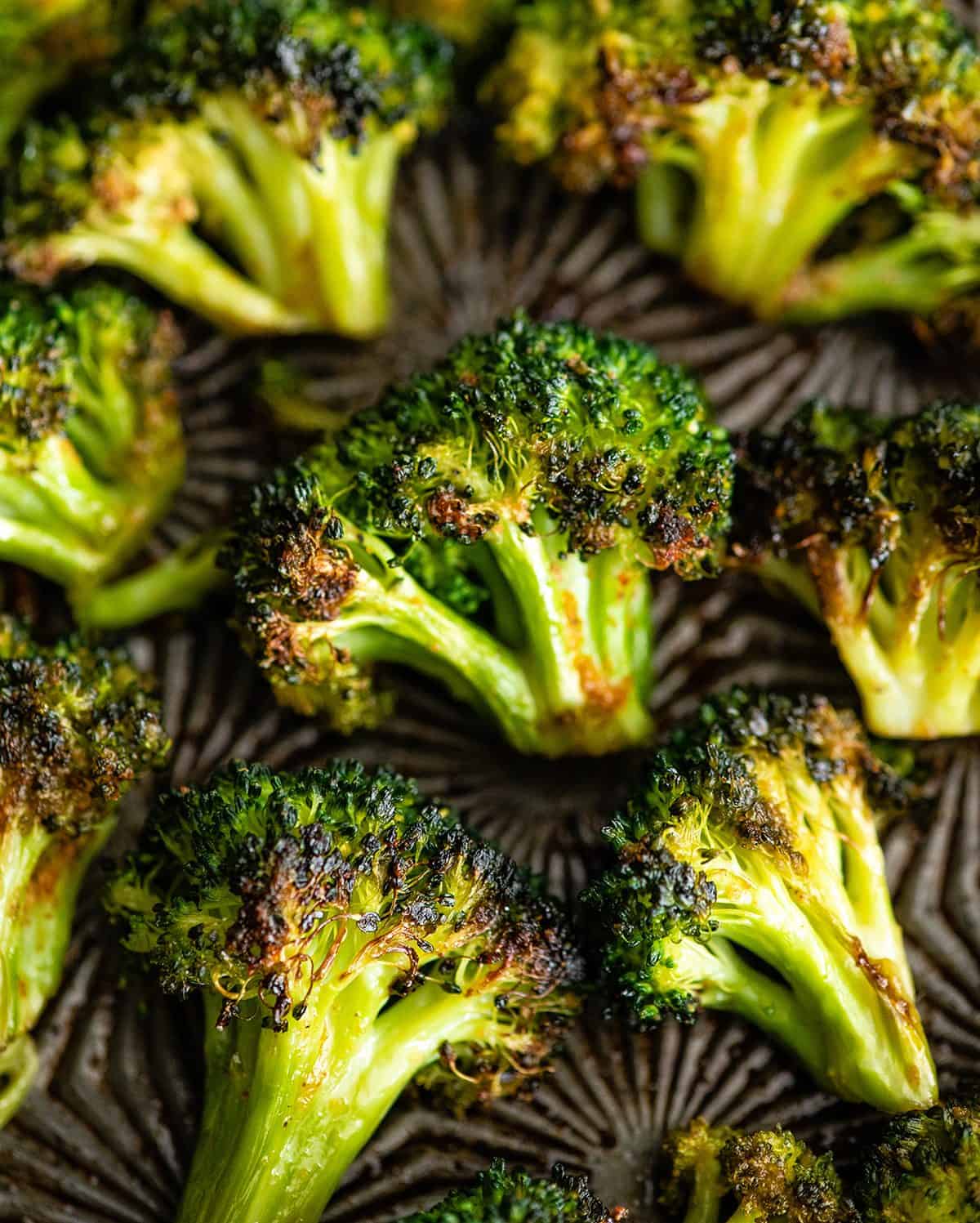 oven roasted broccoli recipe on a metal baking dish - the broccoli is perfectly cooked and is vibrant green with golden brown crispy edges.