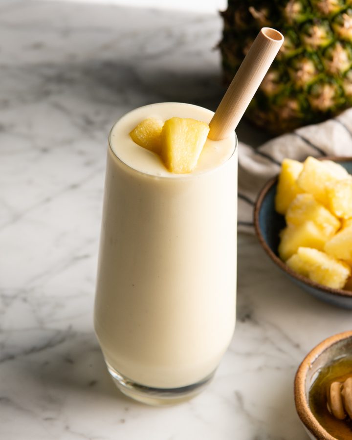 pineapple smoothie in a glass with a straw and two pieces of pineapple on top