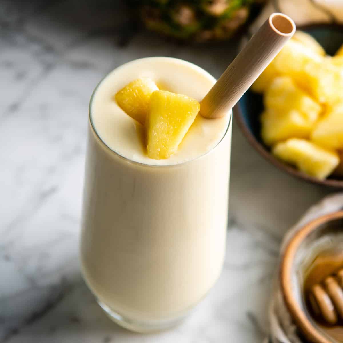 pineapple smoothie in a glass with a straw and pineapple pieces on top