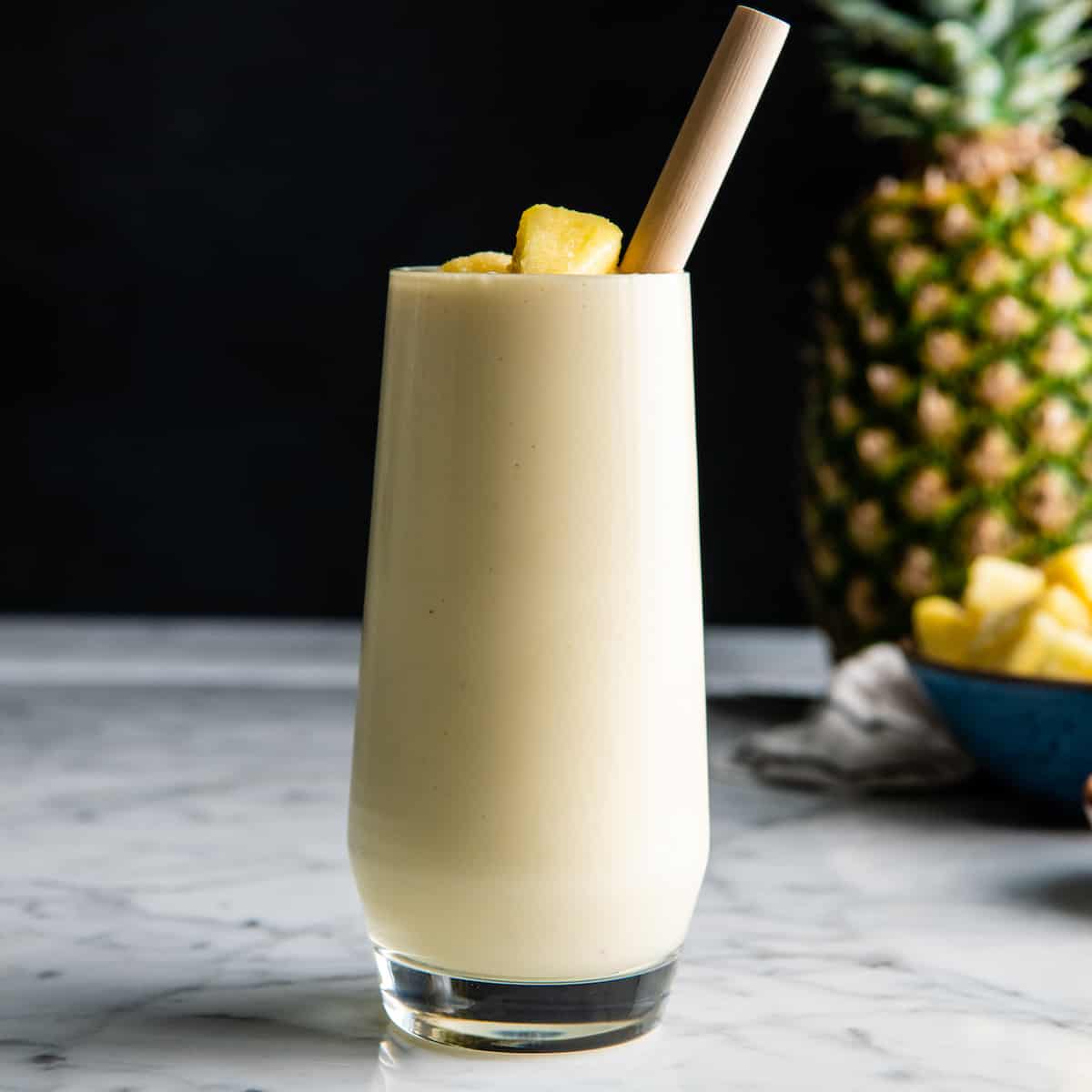 Healthy Pineapple Smoothie in a glass with a straw and pineapple pieces on top
