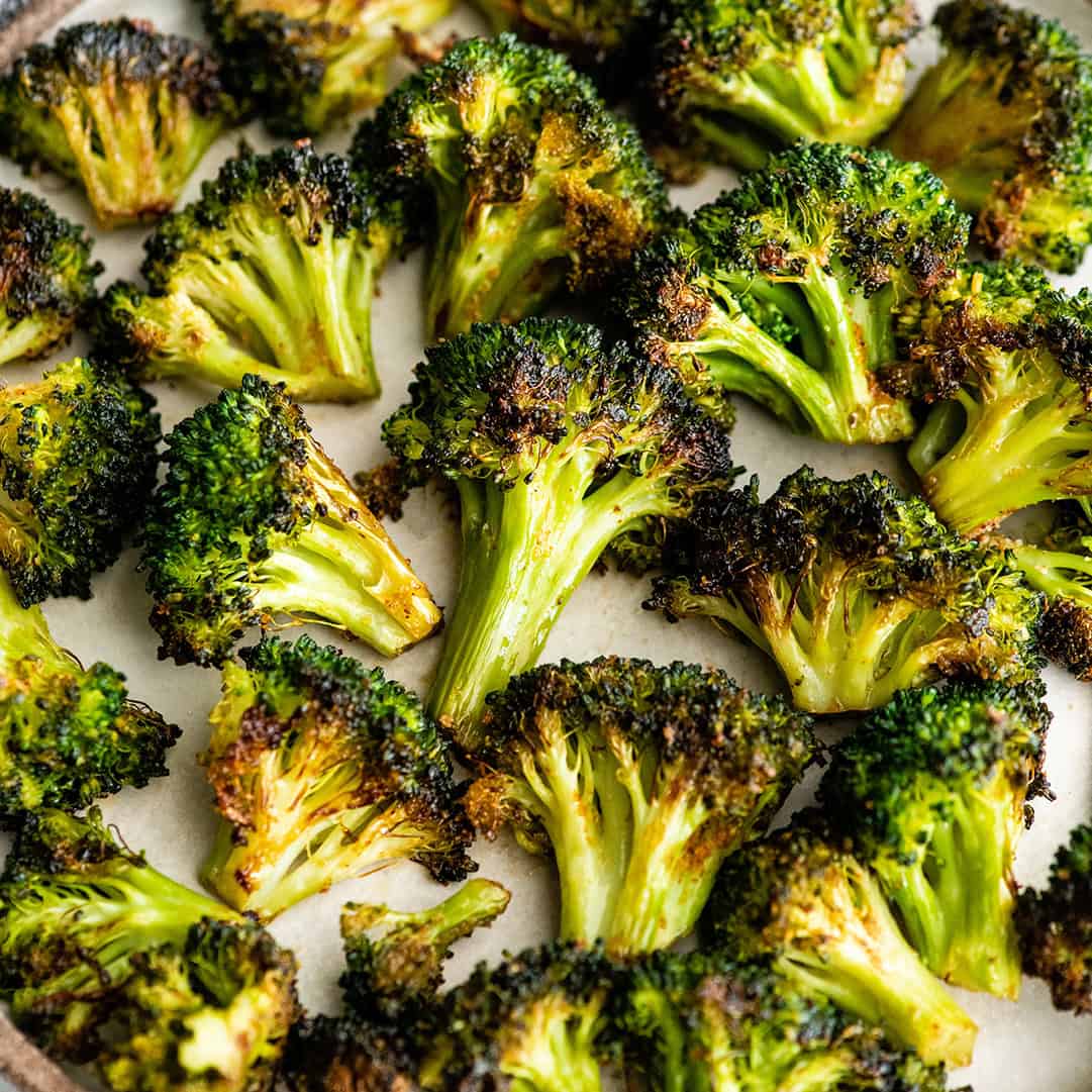 oven roasted broccoli on a plate, the vibrant green roasted broccoli has crispy golden-brown edges.