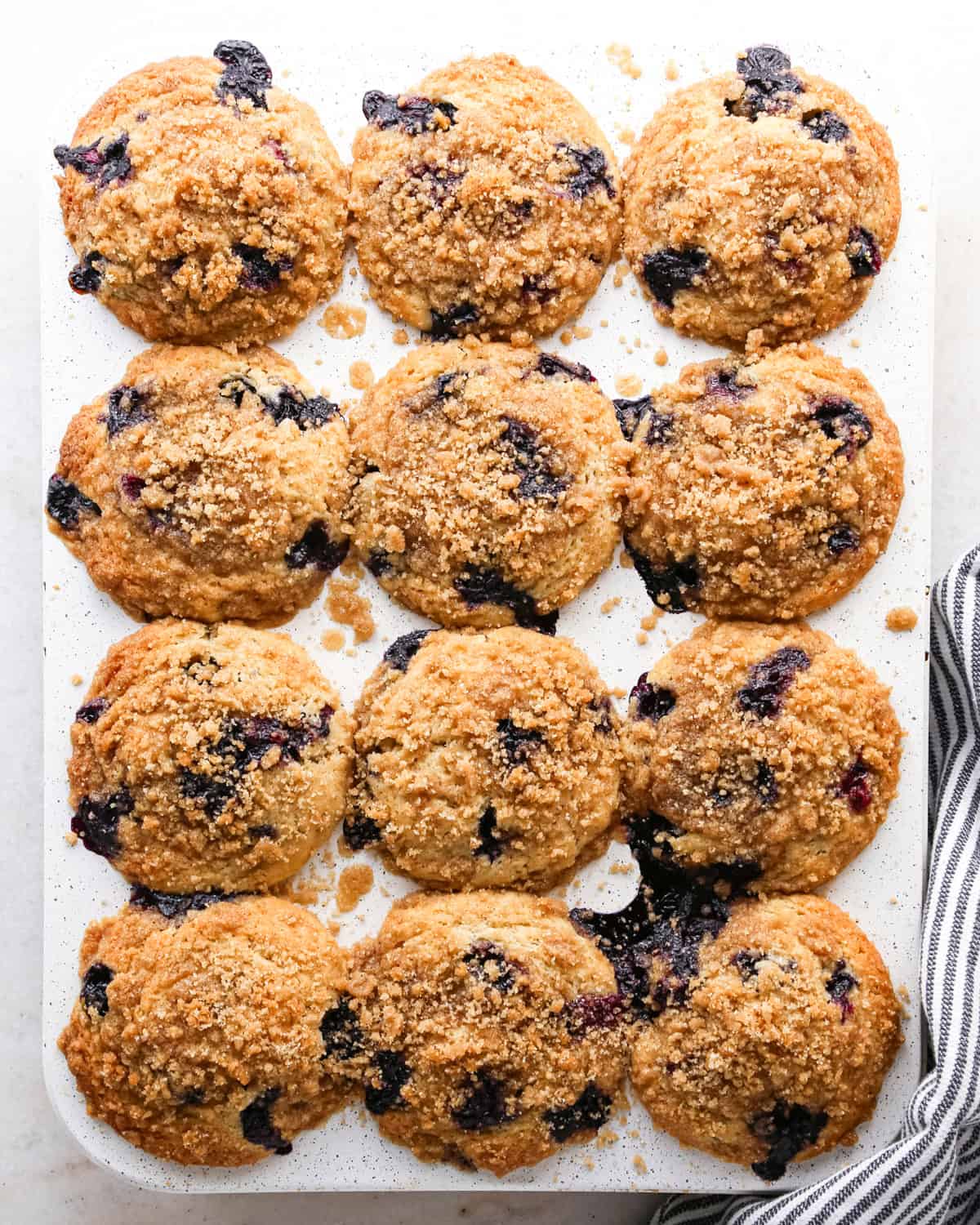 overhead view of 12 baked blueberry muffins in a white muffin tin
