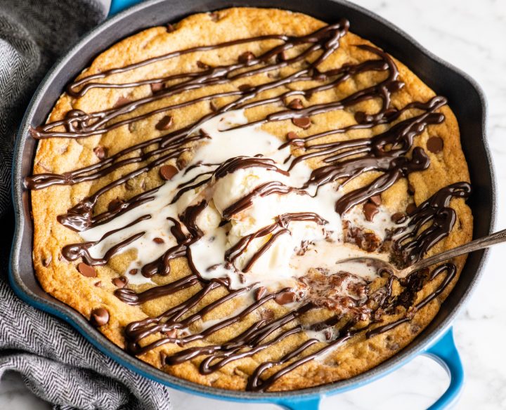 overhead view of a skillet cookie (pizookie) drizzled with chocolate topped with ice cream with a spoon taking a bite