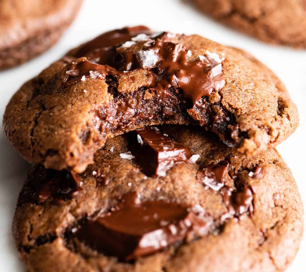 The BEST easy double chocolate chip cookie recipe ever! These chocolate cookies have soft centers, chewy edges and are irresistibly chocolatey. They come together in 5 minutes and require only 30 minutes of chilling time! #chocolate #cookies #chocolatecookies #baking #joyfoodsunshine two double chocolate chip cookies, staked on each other with melty chocolate chunks and sea salt on top. The top cookie has a bite taken out of it so the fudgy gooey texture is visible.