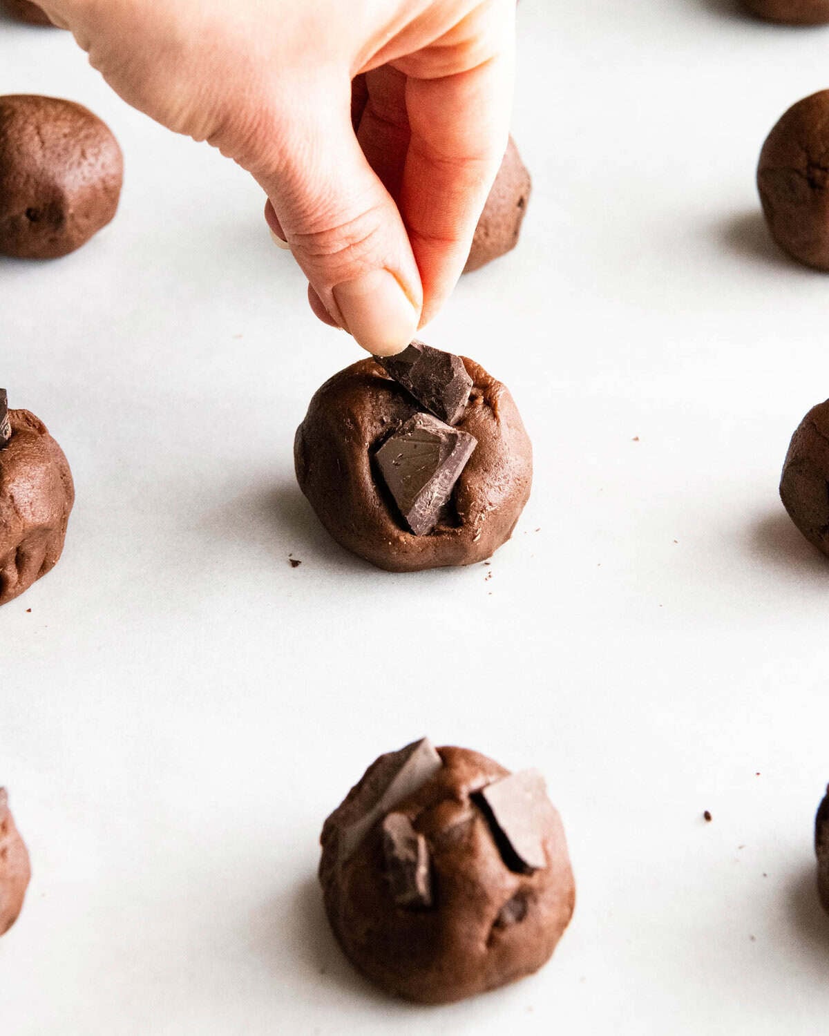 The BEST easy double chocolate chip cookie recipe ever! These chocolate cookies have soft centers, chewy edges and are irresistibly chocolatey. They come together in 5 minutes and require only 30 minutes of chilling time! #chocolate #cookies #chocolatecookies #baking #joyfoodsunshine a hand placing chopped chocolate on top of chocolate cookie dough balls