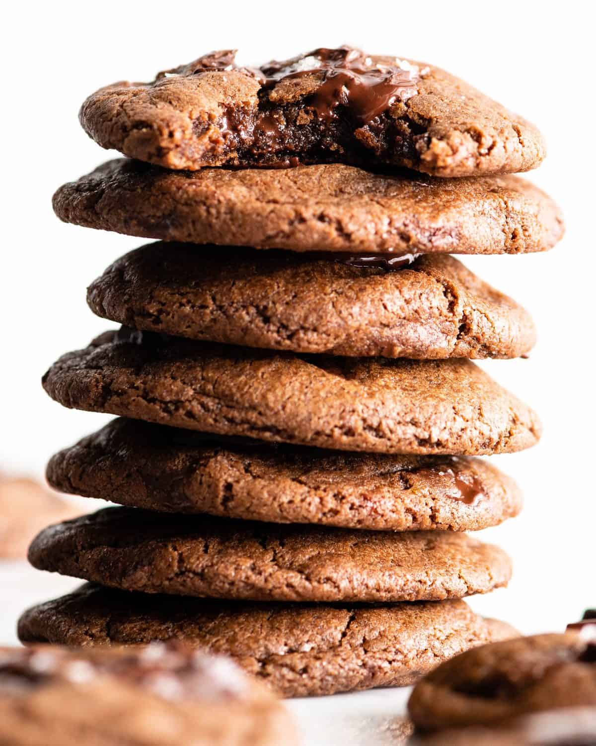 front view of a stack of 7 double chocolate cookies - the top one has a bite taken out of it so the fudgy, rich chocolatey texture is visible