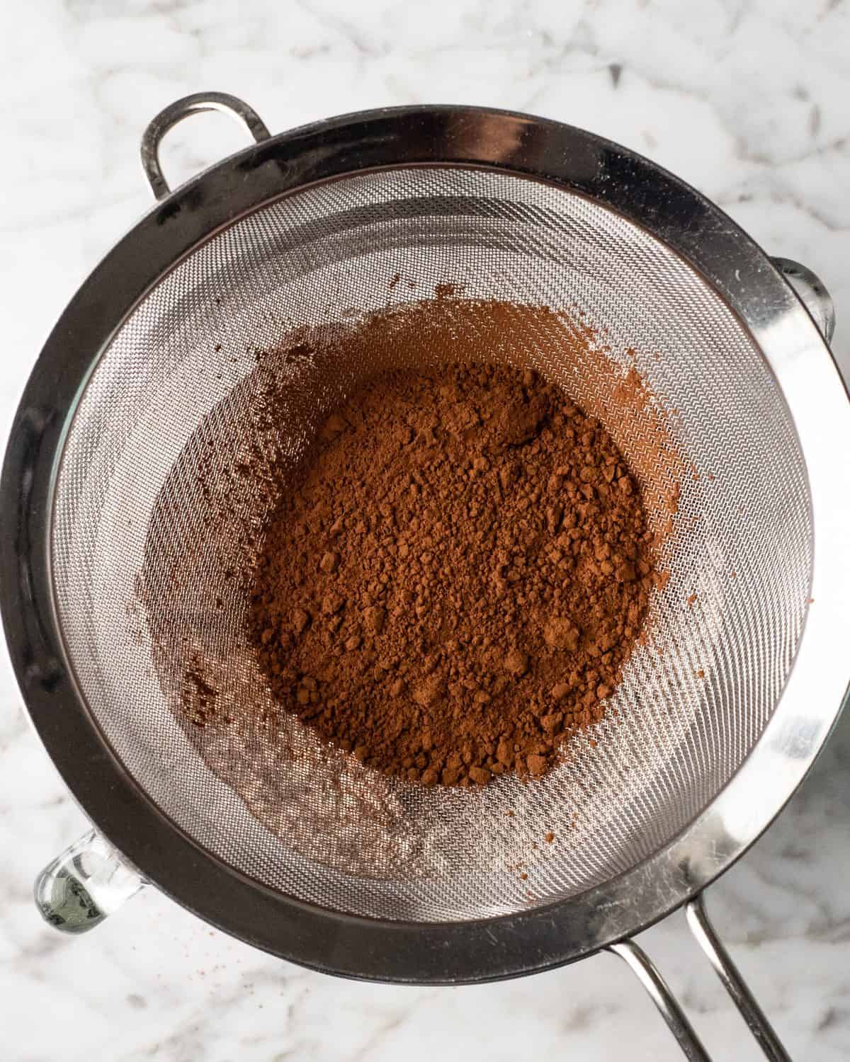 making double chocolate chip cookies - cocoa powder in a fine mesh metal strainer over a glass batter bowl