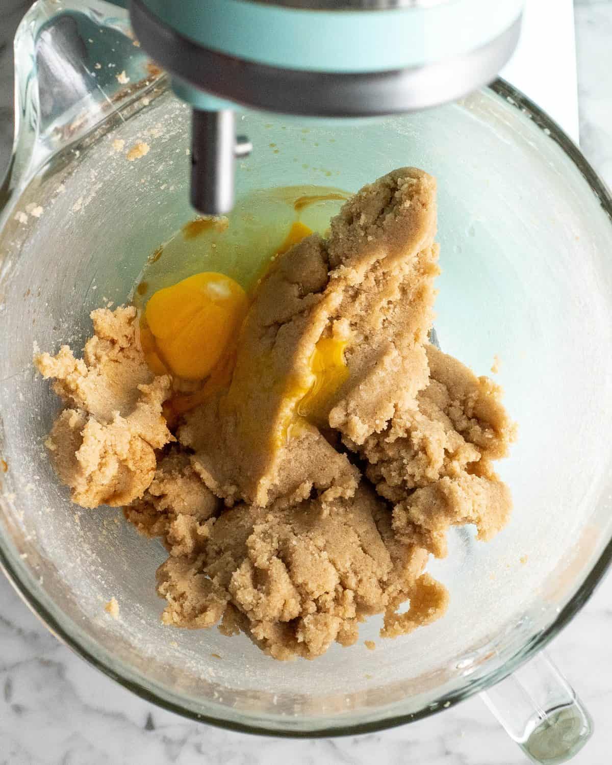 making double chocolate chip cookies - eggs and vanilla added to the beaten butter and sugar mixture in a glass bowl of a light blue standing mixer before mixing
