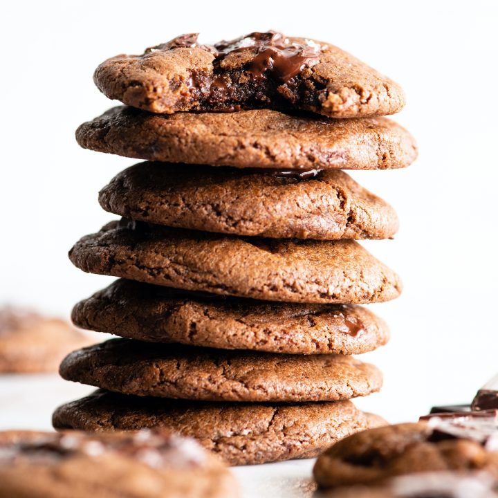 front view of a stack of 7 double chocolate cookies - the top one has a bite taken out of it