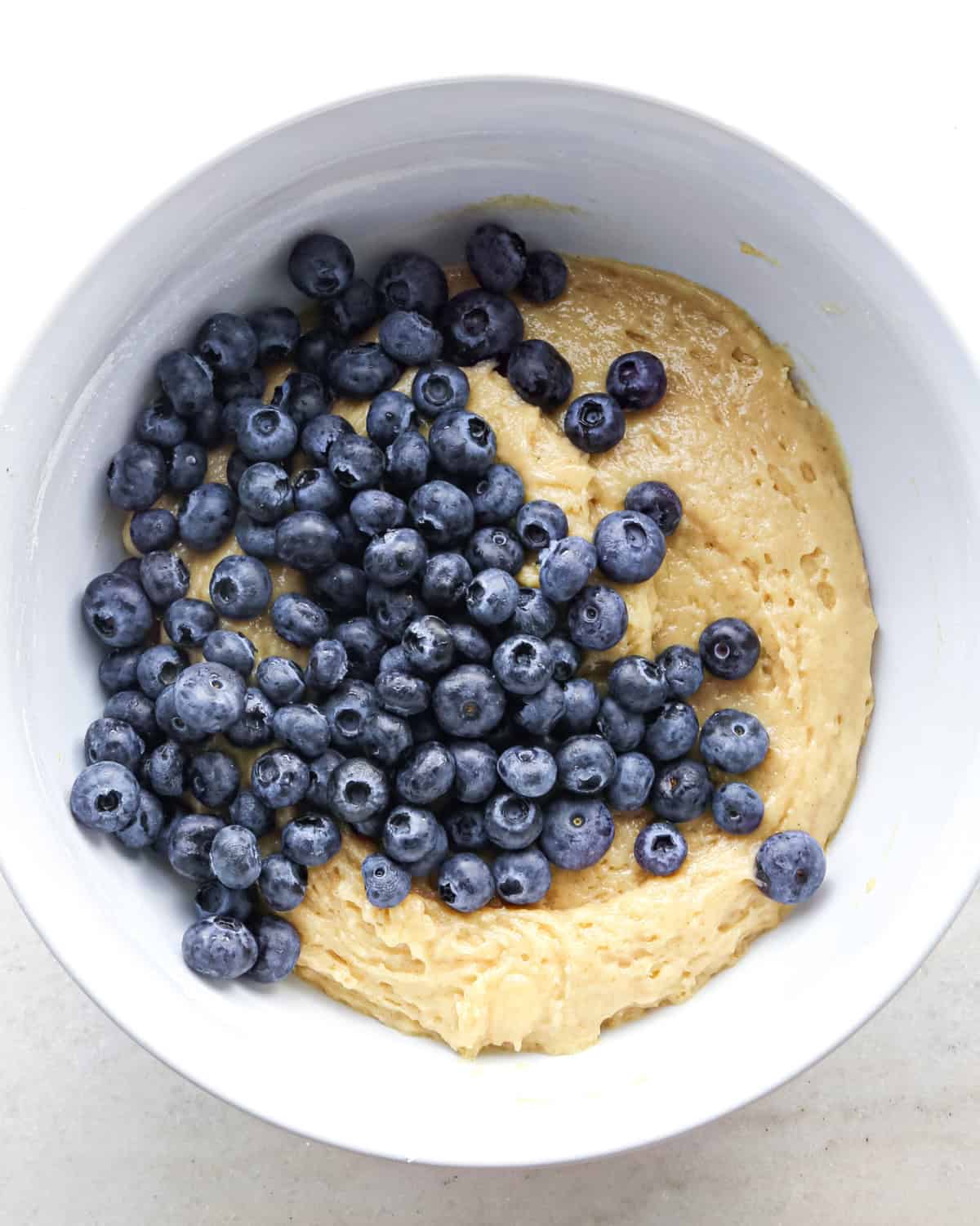 blueberries added to the blueberry muffin batter in a white bowl before mixing