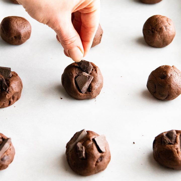 front view of a hand placing chocolate on top of chocolate cookie dough balls
