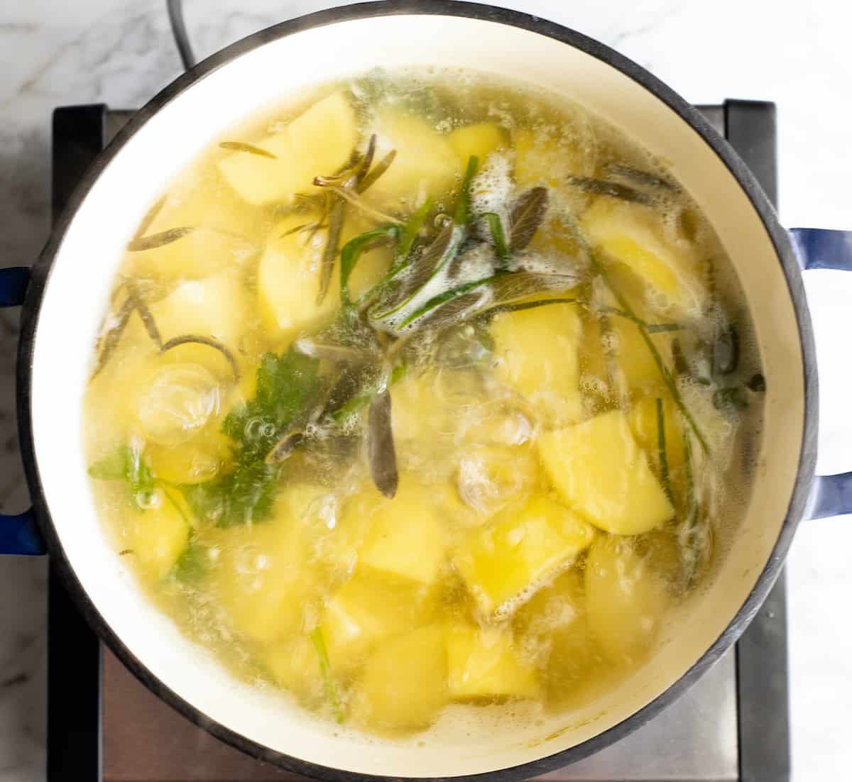 overhead photo showing how to make mashed potatoes - potatoes and herbs boiling in a pot